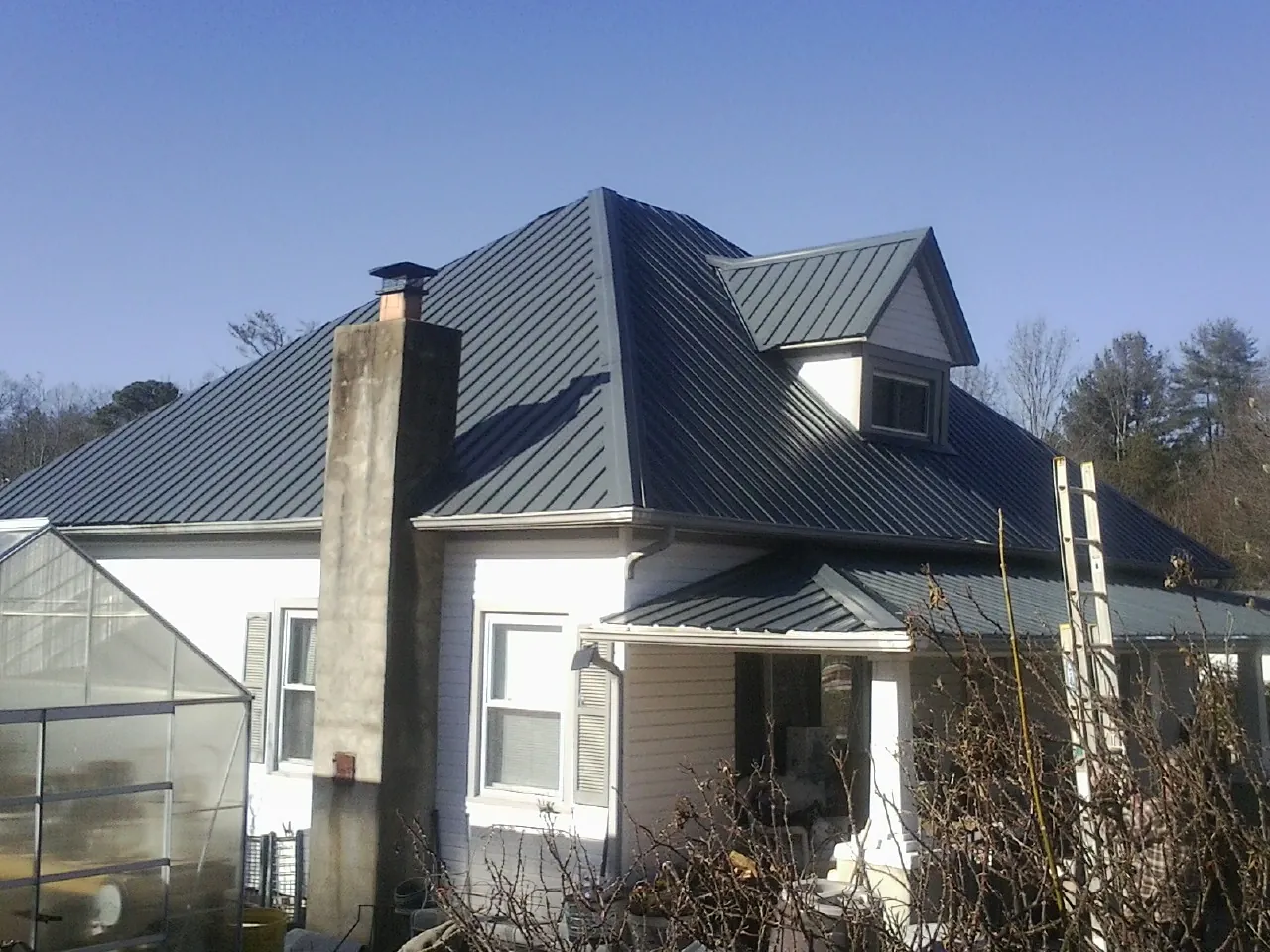 Dark blue standing seam metal roof on a white farmhouse with dormer — Slate & Tile Roof Repair by Roofing Brothers in Beaver Dam
