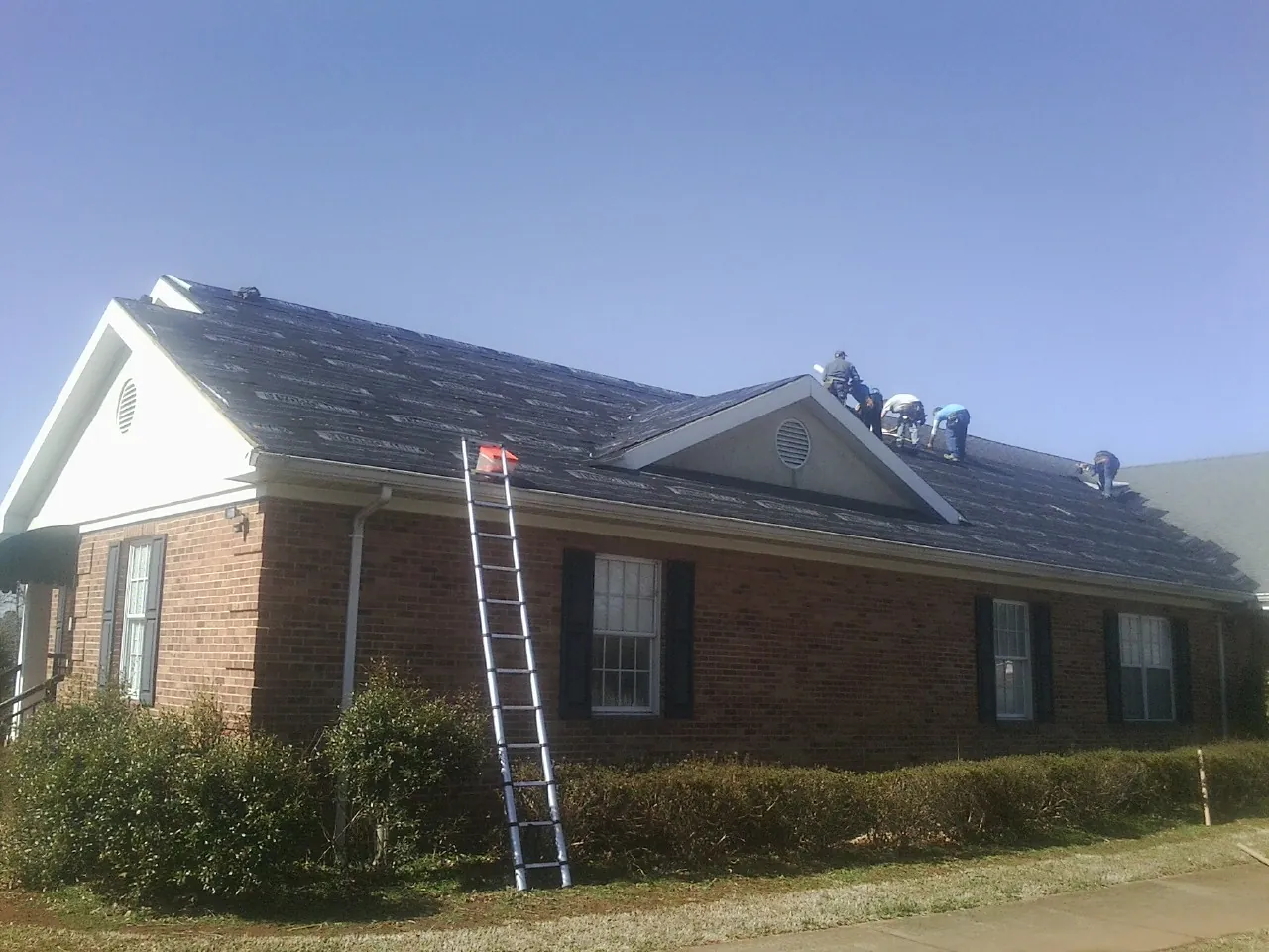 Crew tearing shingles off a brick ranch roof with a ladder set — Emergency Roof Repair work by our crew in Beaver Dam