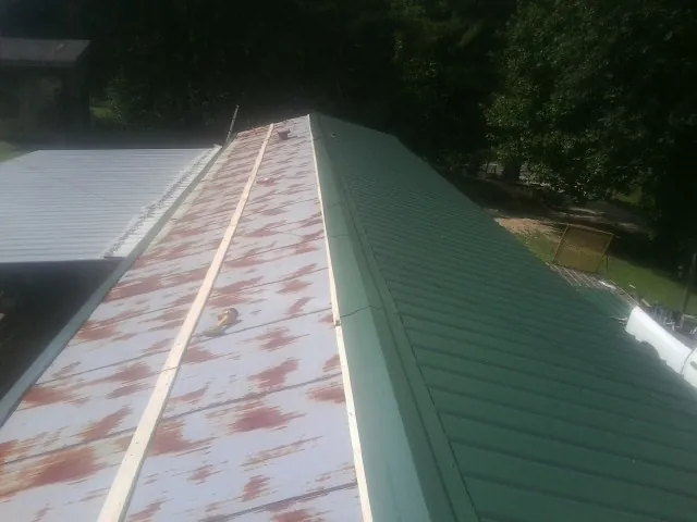 Old rusted panels beside newly installed green metal roofing — Wind Damage Roof Repair by Roofing Brothers in Beaver Dam