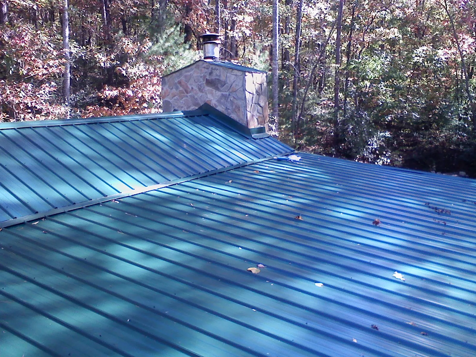 New green metal roof and stone chimney surrounded by autumn woods in Beaver Dam